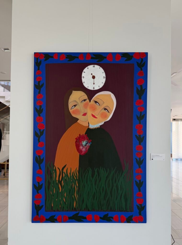 Painting of two women embracing beneath a clock, framed by a blue border of red flowers, at the Unpromised Flowers exhibition